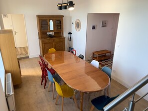 A dining area with a wooden table, colorful chairs, a wooden cabinet, and a small shelf.