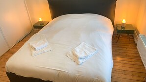 A neatly made bed with white linens and two folded towels on the bed. There are two bedside tables with candles on them. - Wimereux: Large house ideally located 🏖, Les Arômes (Wimereux)