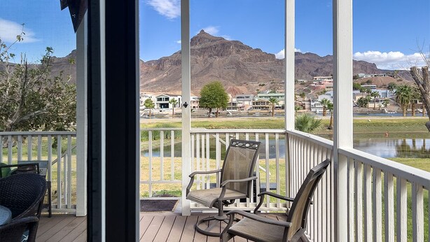 Un espacio al aire libre techado con dos sillas y una mesa, con vistas a un cuerpo de agua y un paisaje montañoso.