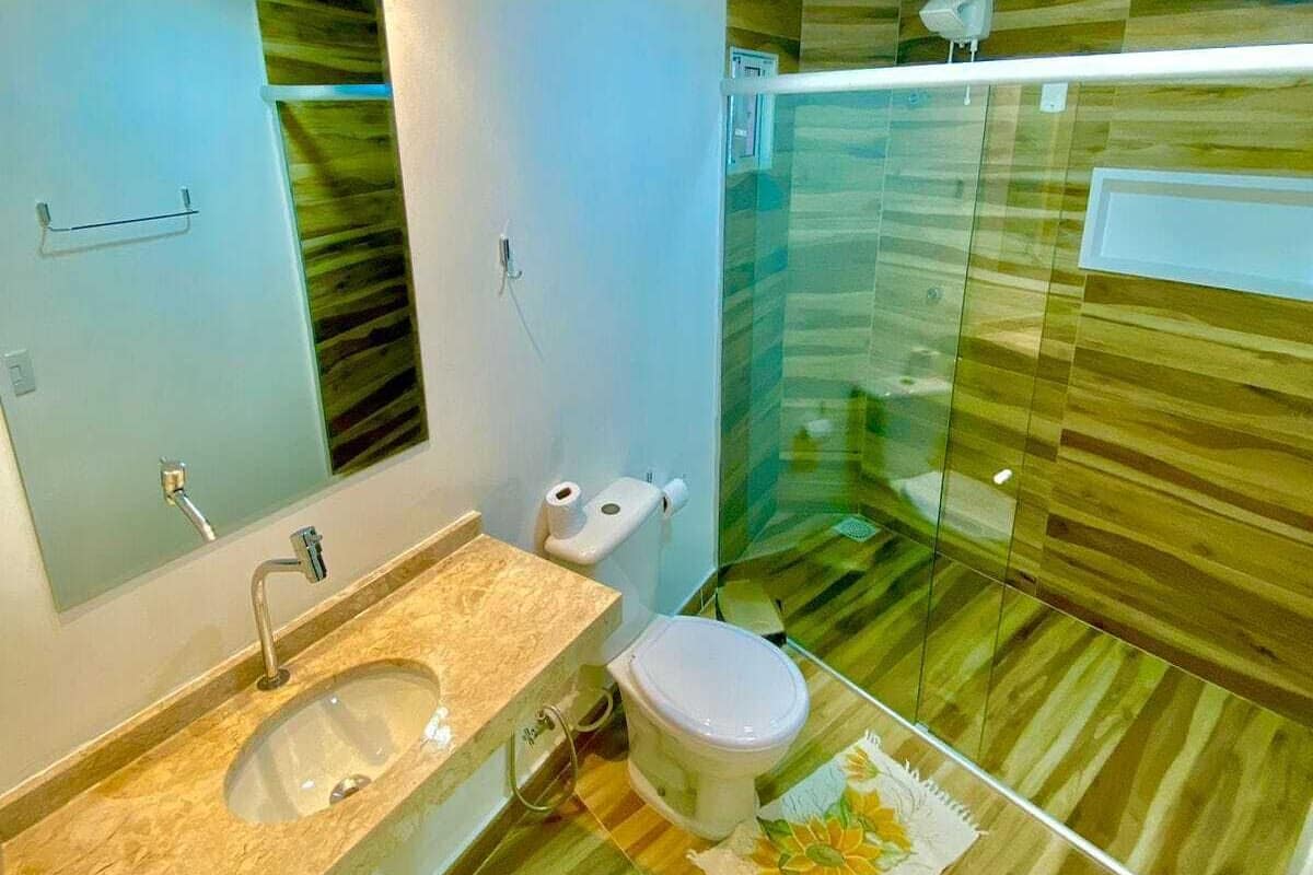 Casa de banho moderna com cabine de duche em vidro, lavatório com bancada de mármore e sanita.