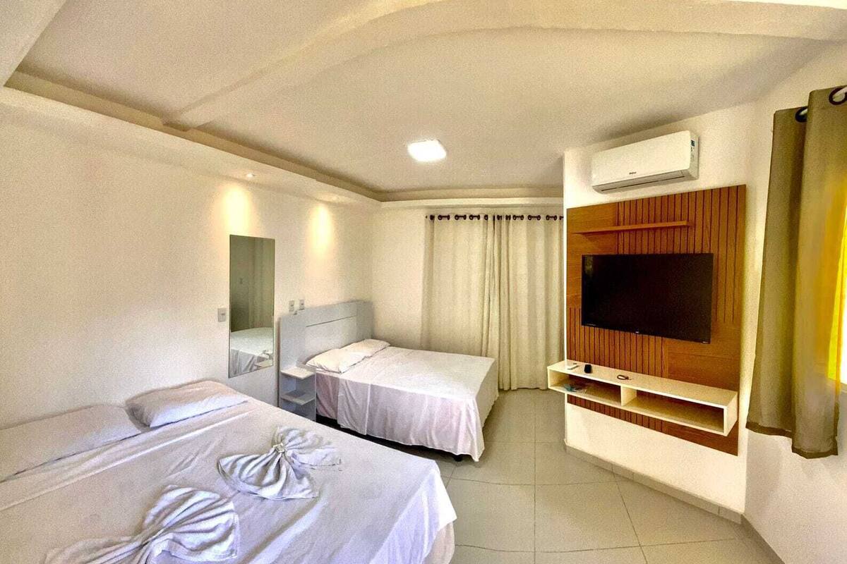 Quarto de hotel com duas camas, uma televisão e ar condicionado.