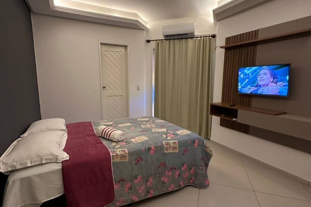 Quarto com cama, televisão na parede e uma porta.