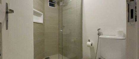 Un baño con ducha de vidrio, inodoro y un pequeño cubo de basura.