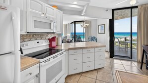 Una cocina moderna con armarios blancos, una estufa y vista a la playa a través de una puerta de vidrio.