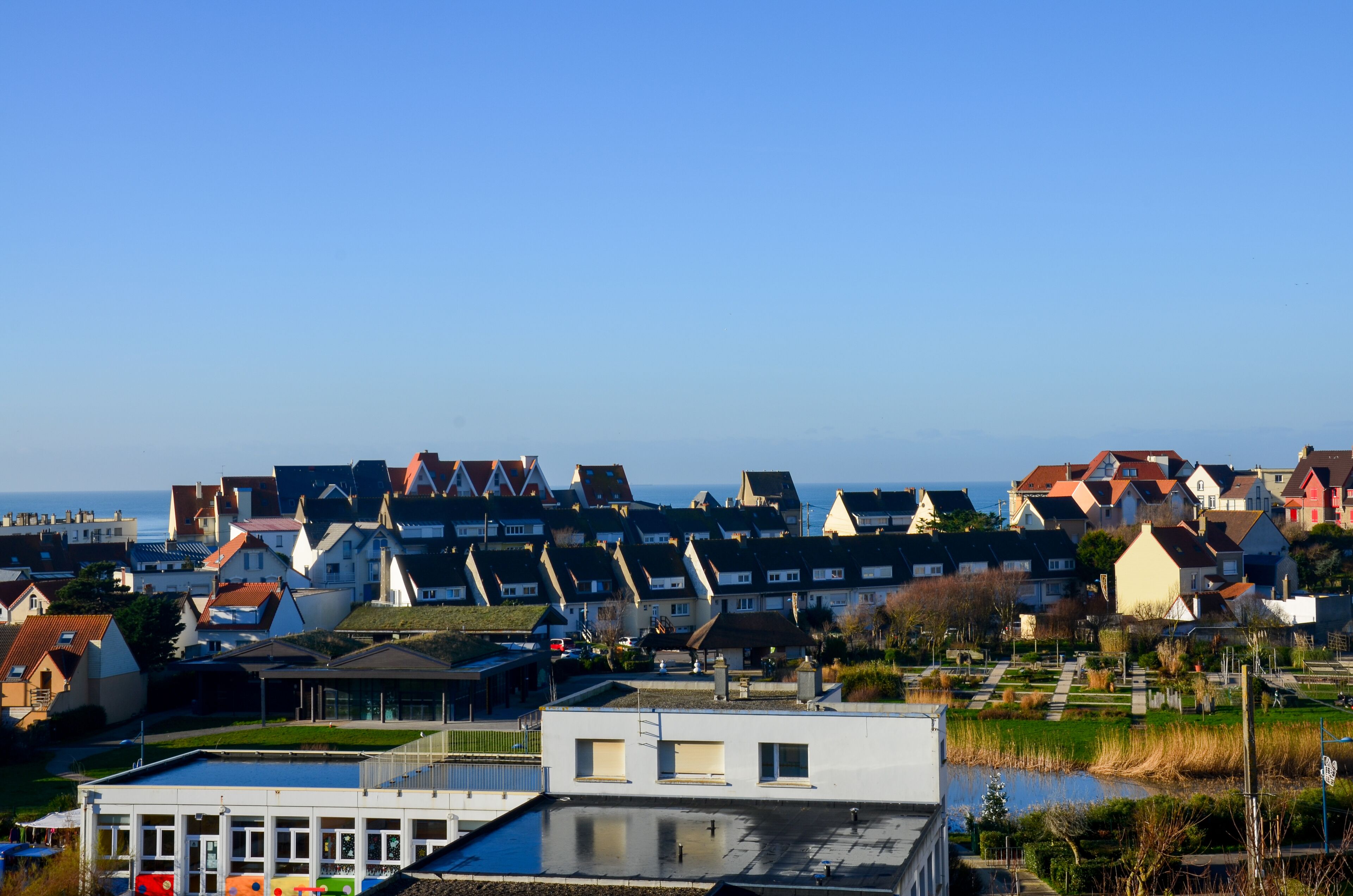 A coastal residential area with houses, a small body of water, and a modern building with a flat roof.