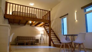 A spacious living area with a high wooden staircase, a sofa, two chairs, and a table. - Uni Island City Suites (Heraklion)