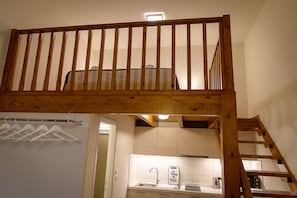 Cozy loft-style bedroom with a staircase leading to an upper sleeping area, featuring a kitchenette with sink and kettle.