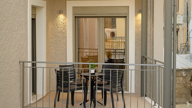 A two-story building with a balcony featuring a table and chairs, a door leading to an interior space, and a small garden area above. - Uni Island City Suites (Heraklion)