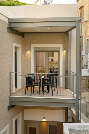 A two-story building with a balcony featuring a table and chairs, a door leading to an interior space, and a small garden area above. - Uni Island City Suites (Heraklion)
