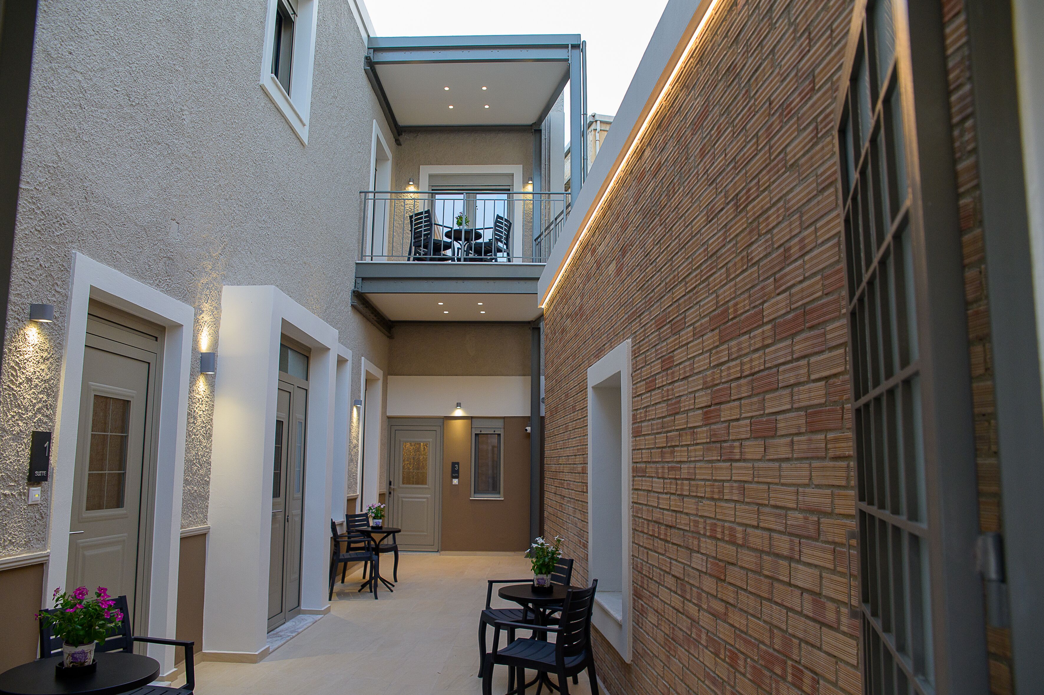 Een smalle, buitenste gang met een bakstenen muur aan één kant en een balkon met tafel en stoelen aan de andere kant.