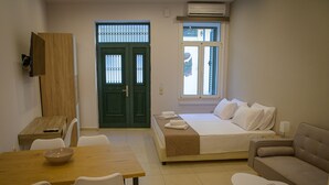 A hotel room with a bed, a sofa, a dining table, and a small table with a bowl. - Uni Island City Suites (Heraklion)