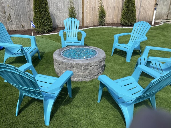 A circular seating area with six blue Adirondack chairs around a stone fire pit. - Captain Alexander’s Spa & Putting Green not a vacation home but a destination. (West Harwich)