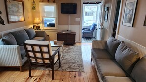 A cozy living room with a wooden ceiling, a flat-screen TV, a sofa, a chair, and a small table.