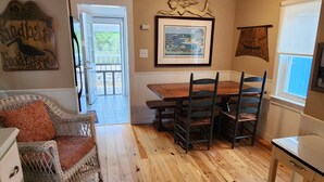 A wooden-floored dining area with a table and chairs, a wicker chair, and a white cabinet.