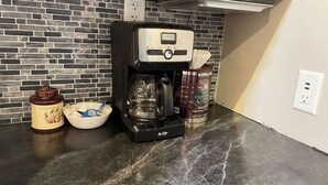 A coffee maker on a kitchen counter with a brick-patterned backsplash, a jar, and a bowl.