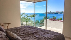 A bedroom with a large bed and a view of the sea through floor-to-ceiling glass windows. - 2063 - Lu Iba Condo 2 (Santa María Huatulco)