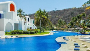 A resort with a large swimming pool, palm trees, and a white building with arched windows. - 2063 - Lu Iba Condo 2 (Santa María Huatulco)