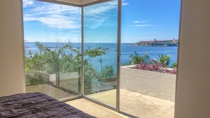 A bedroom with a large sliding glass door leading to a balcony with a view of the sea and a distant island. - 2064 - Residencias Lu Iba Condo 4 (Santa María Huatulco)