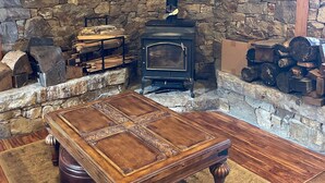 A cozy room with a stone wall, a wood-burning stove, a wooden table, and a rug. - Majestic Mountain Escape (Placerville)