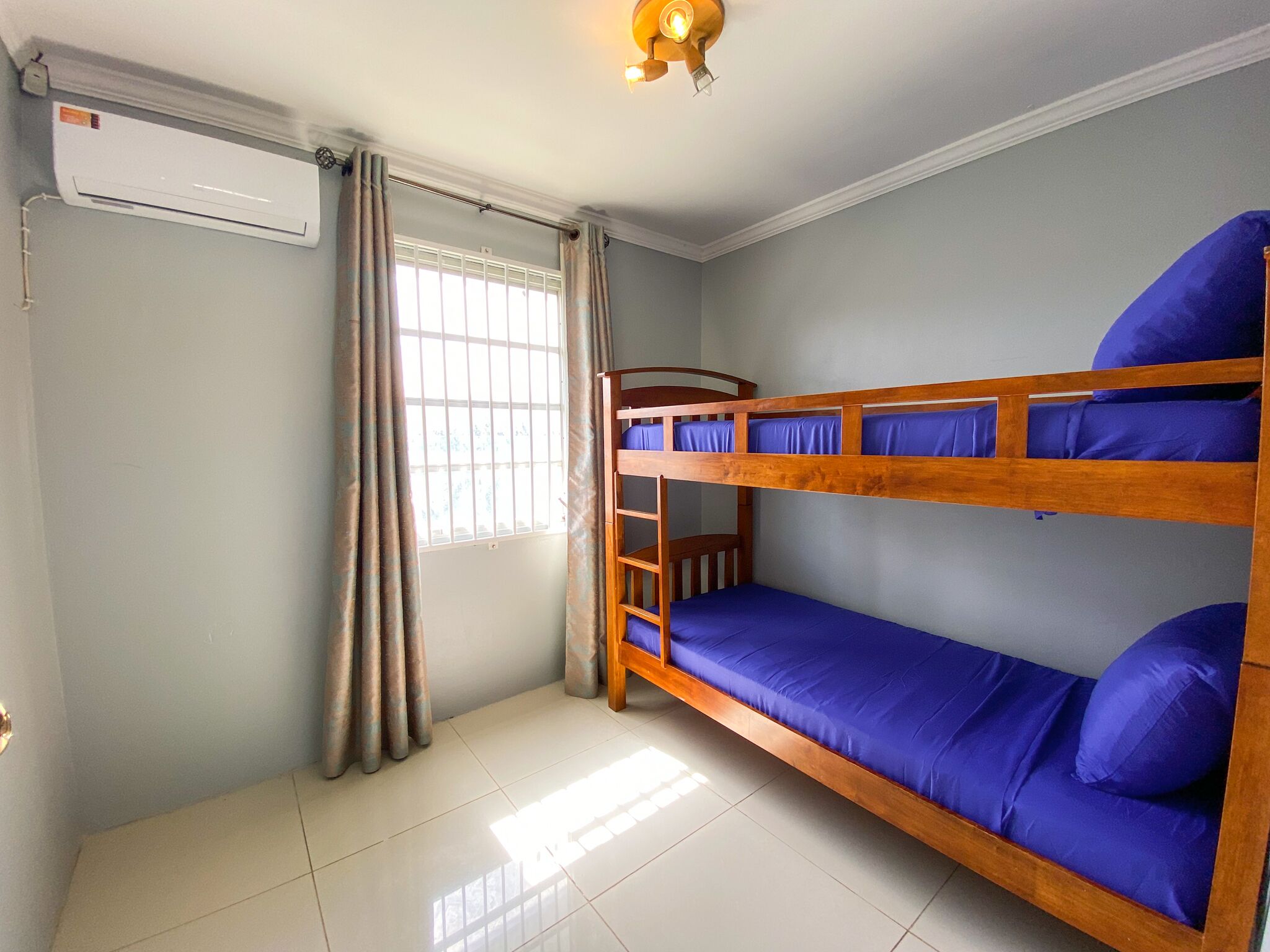 A room with bunk beds, a window with curtains, an air conditioning unit, and a ceiling light fixture.