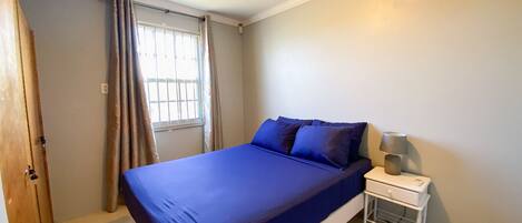 A bedroom with a bed, a nightstand, a window with curtains, and an air conditioning unit.