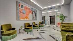 Een moderne lobby met een groot kunstwerk met een valutathema, groene bekleden stoelen en een marmeren vloer.