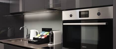 A modern kitchen with a built-in oven, a coffee maker, and a tea station.