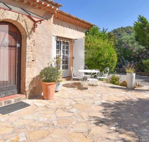 Un patio de piedra con una mesa y sillas, una planta en maceta y un edificio con tejado de tejas y una puerta.