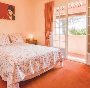 Un dormitorio con cama, mesita de noche, un cuadro en la pared y ventana con cortinas.