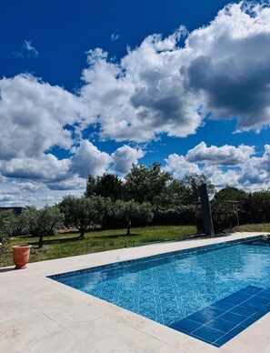 Una piscina bajo un cielo azul despejado y algunas nubes.