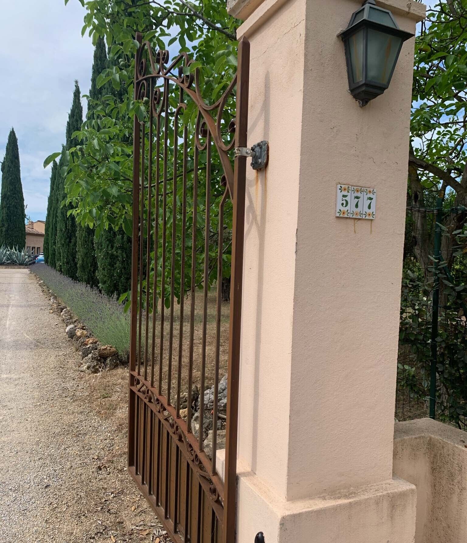 A gated entrance with a metal gate, a beige wall, and a number plate.