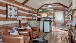 A cozy cabin interior with a wooden interior, a dining table, two leather chairs, a refrigerator, and a kitchen area with a sink and stove. - Cozy Cabin for Two 1 Block to Main (Fredericksburg)