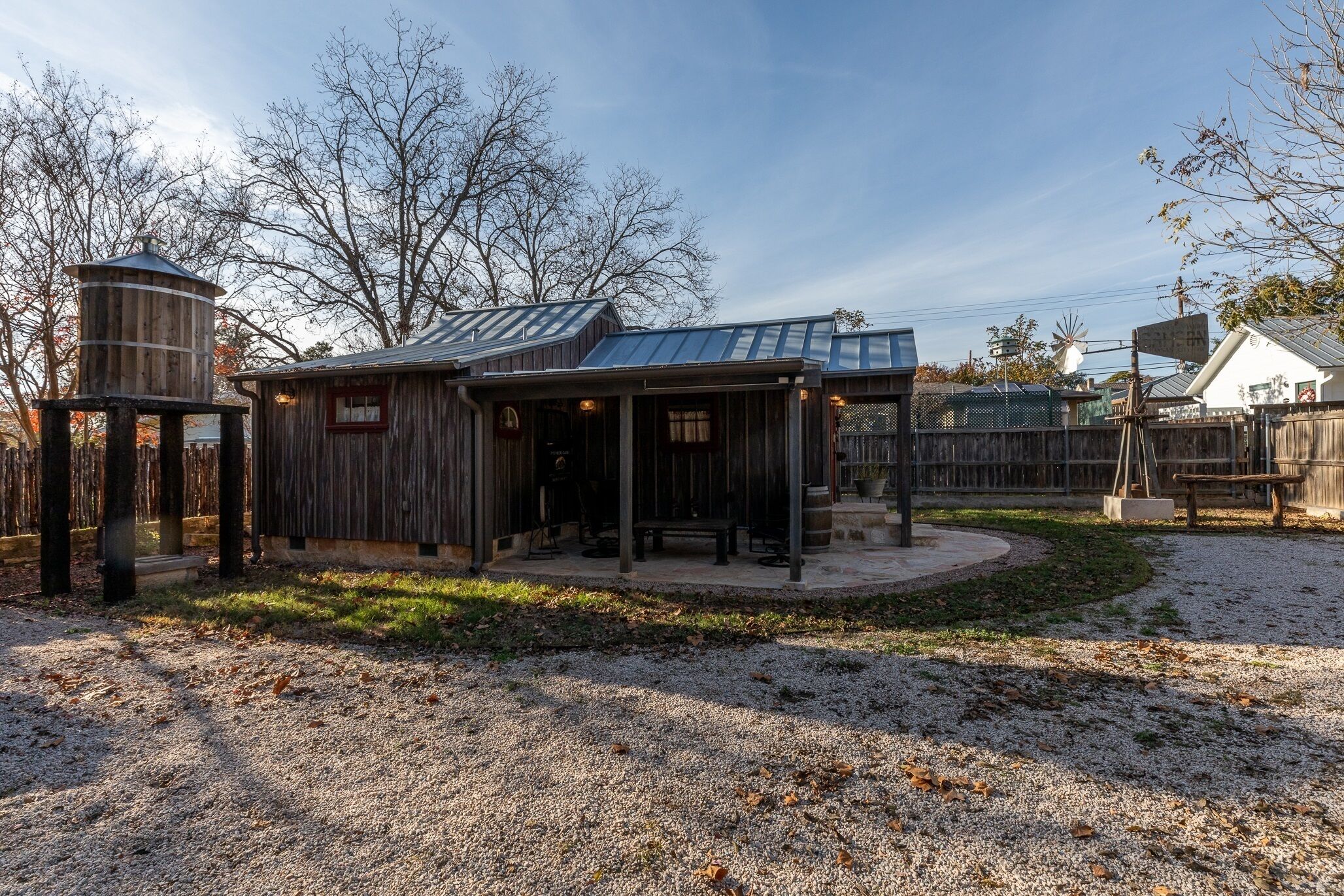 A rustic wooden cabin with a metal roof, a water tower, and a fenced yard with a bench and picnic table.
