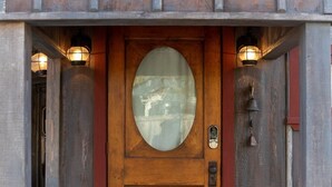 A rustic wooden building with a circular glass door, a metal fan-like structure above the door, and two wall-mounted lanterns. - Cozy Cabin for Two 1 Block to Main (Fredericksburg)