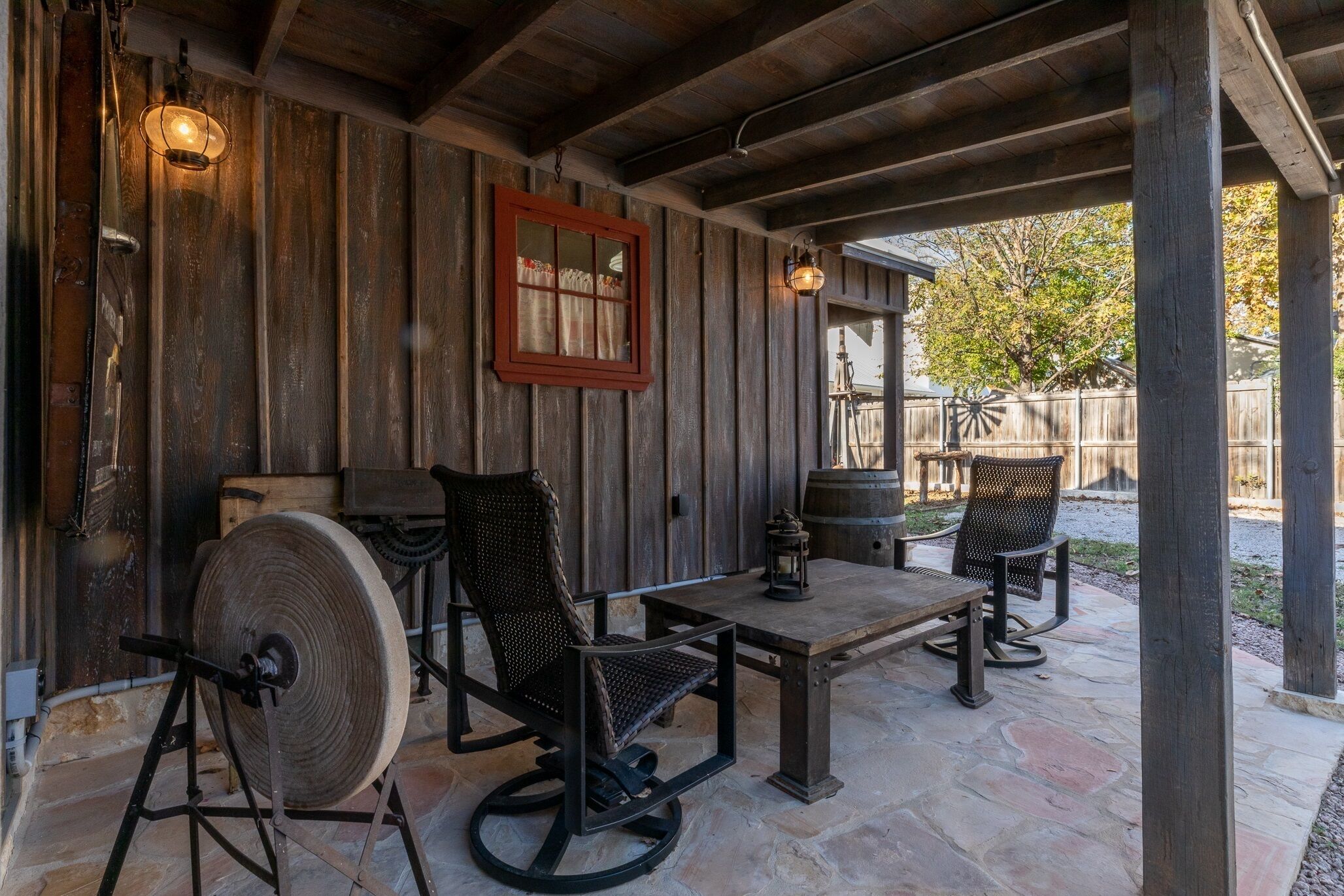Une terrasse extérieure avec des murs en bois rustique, un sol en pierre et une table entourée de chaises.