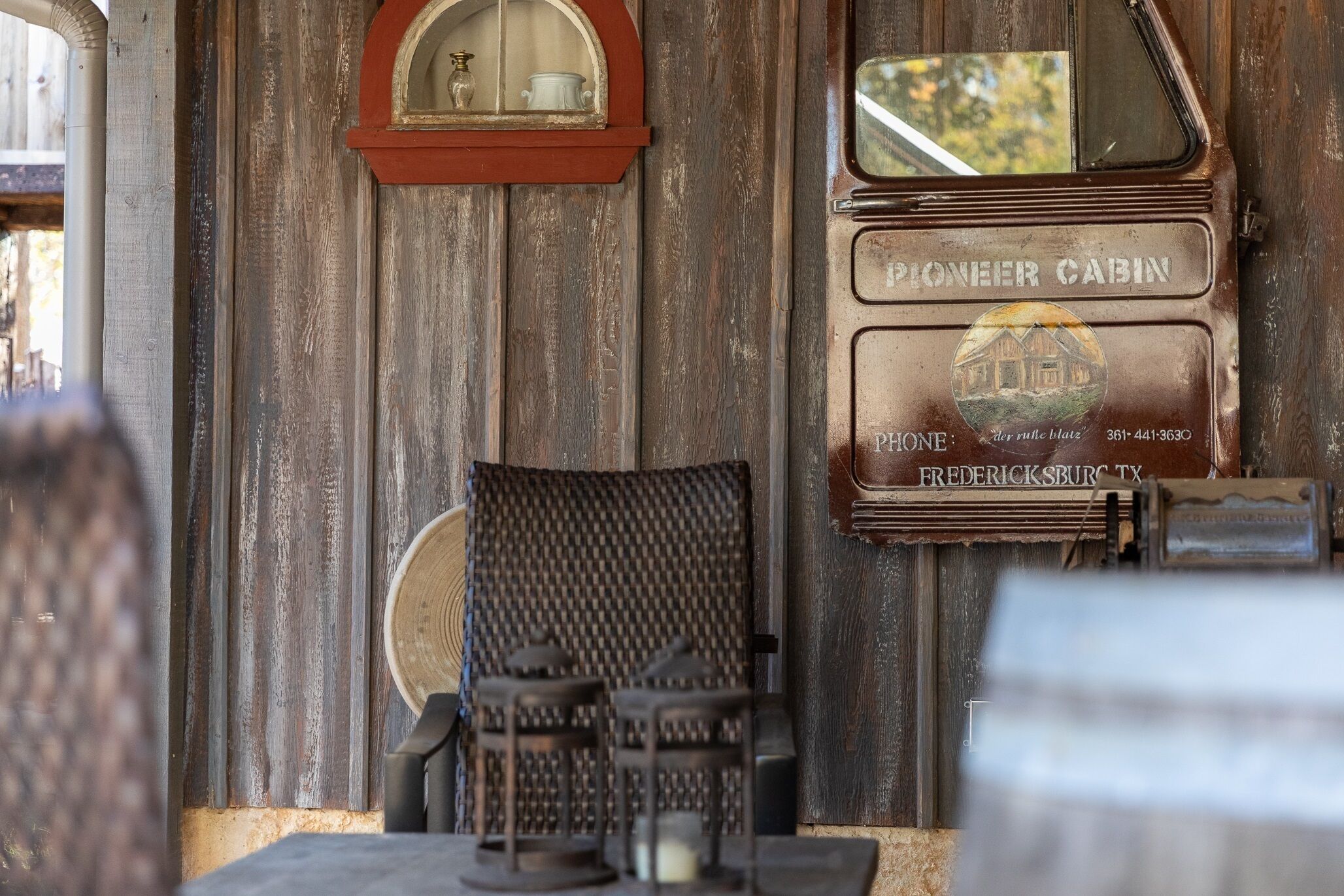 A rustic wooden wall with a vintage Pioneer Cafe sign, a telephone, and a wicker chair.