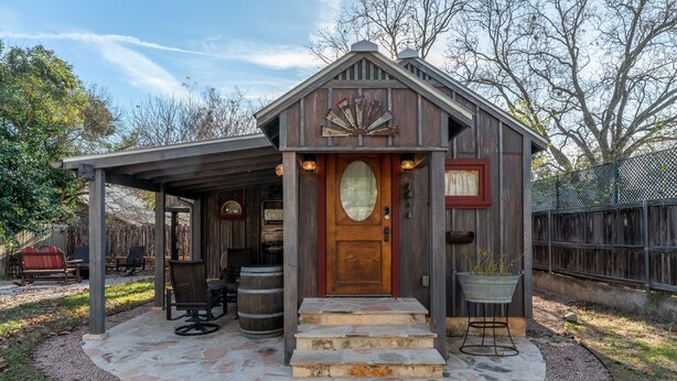 A rustic cabin with a stone-paved entrance, wooden porch, and outdoor seating area. - Cozy Cabin for Two 1 Block to Main (Fredericksburg)