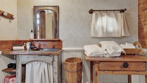 A rustic bathroom with a wooden vanity, a mirror, a towel rack, and a wooden bucket. - Cozy Cabin for Two 1 Block to Main (Fredericksburg)