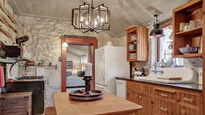 Una cocina rústica con pared de piedra, armarios de madera, una isla central y una estufa antigua.