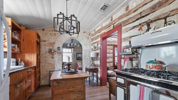 A rustic kitchen with wooden cabinets, a stone wall, and a vintage stove. - *Best Location* Haus + Cabin 1 block 2 Main HOT TUB and Firepit EV Charger (Fredericksburg)
