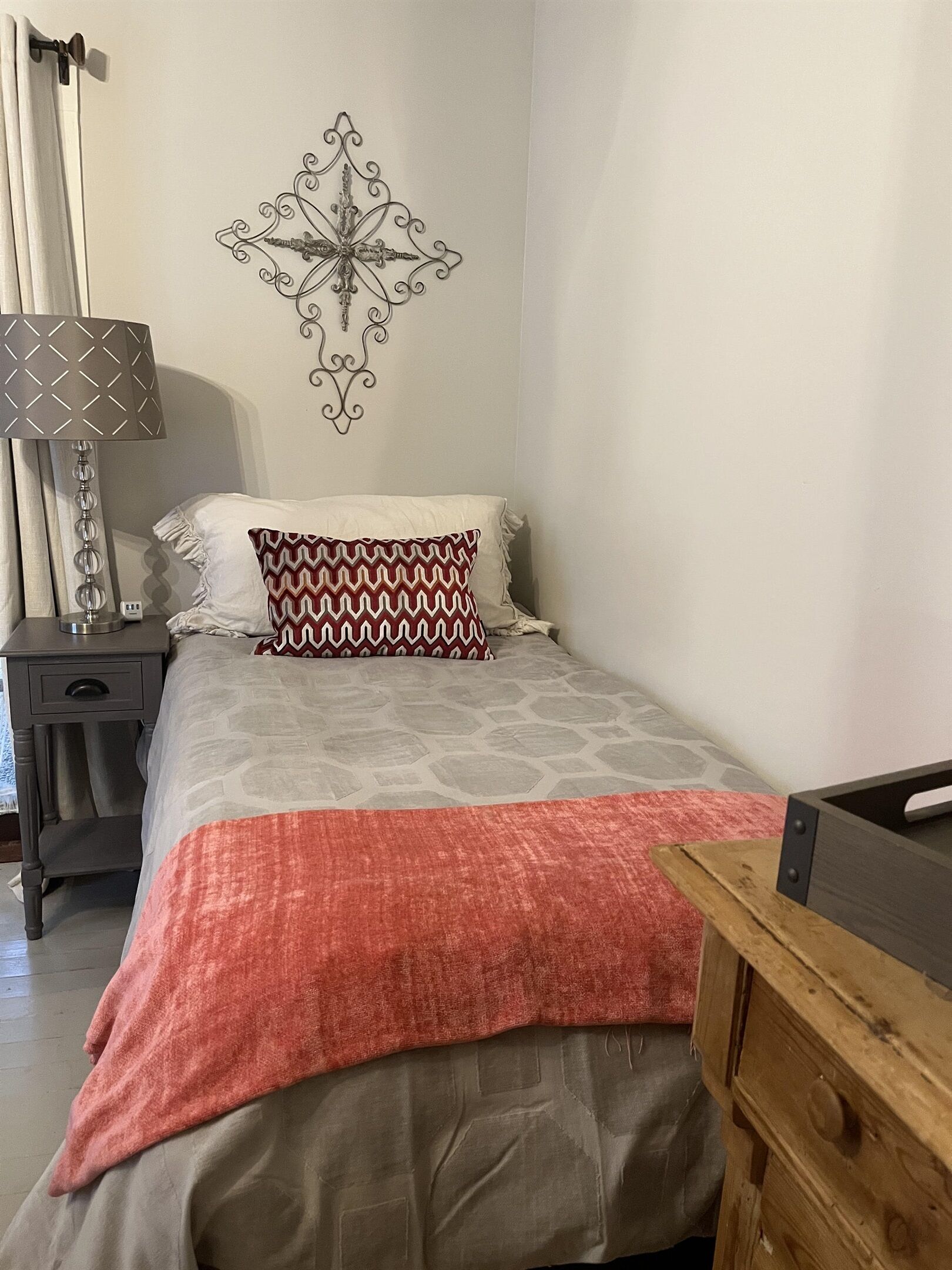Un dormitorio con cama, mesita de noche, lámpara, un adorno en la pared y cómoda de madera.