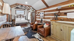 A rustic room with a bed, leather chairs, a wooden table, and a sink. - *Best Location* Haus + Cabin 1 block 2 Main HOT TUB and Firepit EV Charger (Fredericksburg)