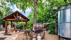 A rustic outdoor setting with a wooden pavilion, a large barrel, and a metal tank. - *Best Location* Haus + Cabin 1 block 2 Main HOT TUB and Firepit EV Charger (Fredericksburg)