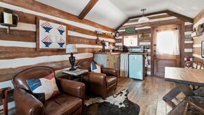 A rustic cabin interior with wooden walls, a dining table, leather chairs, a small kitchenette, and a cowhide rug. - *Best Location* Haus + Cabin 1 block 2 Main HOT TUB and Firepit EV Charger (Fredericksburg)