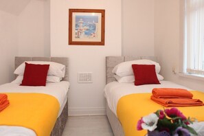 A hotel room with two beds, each with a red pillow and a yellow blanket. There is a framed picture on the wall above the beds.