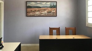 Un comedor con mesa y sillas, un ventilador de techo y un cuadro de paisaje en la pared.