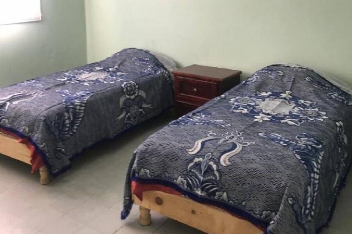 A room with two single beds, a small wooden nightstand, a ceiling fan, and a window with blinds.