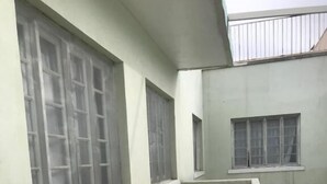 Un pasillo con suelo de baldosas, un muro de contención de hormigón y varias ventanas con rejas de metal.