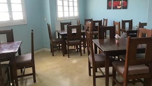 Un área de comedor con varias mesas y sillas de madera, paredes azul claro y un ventanal con marcos blancos.