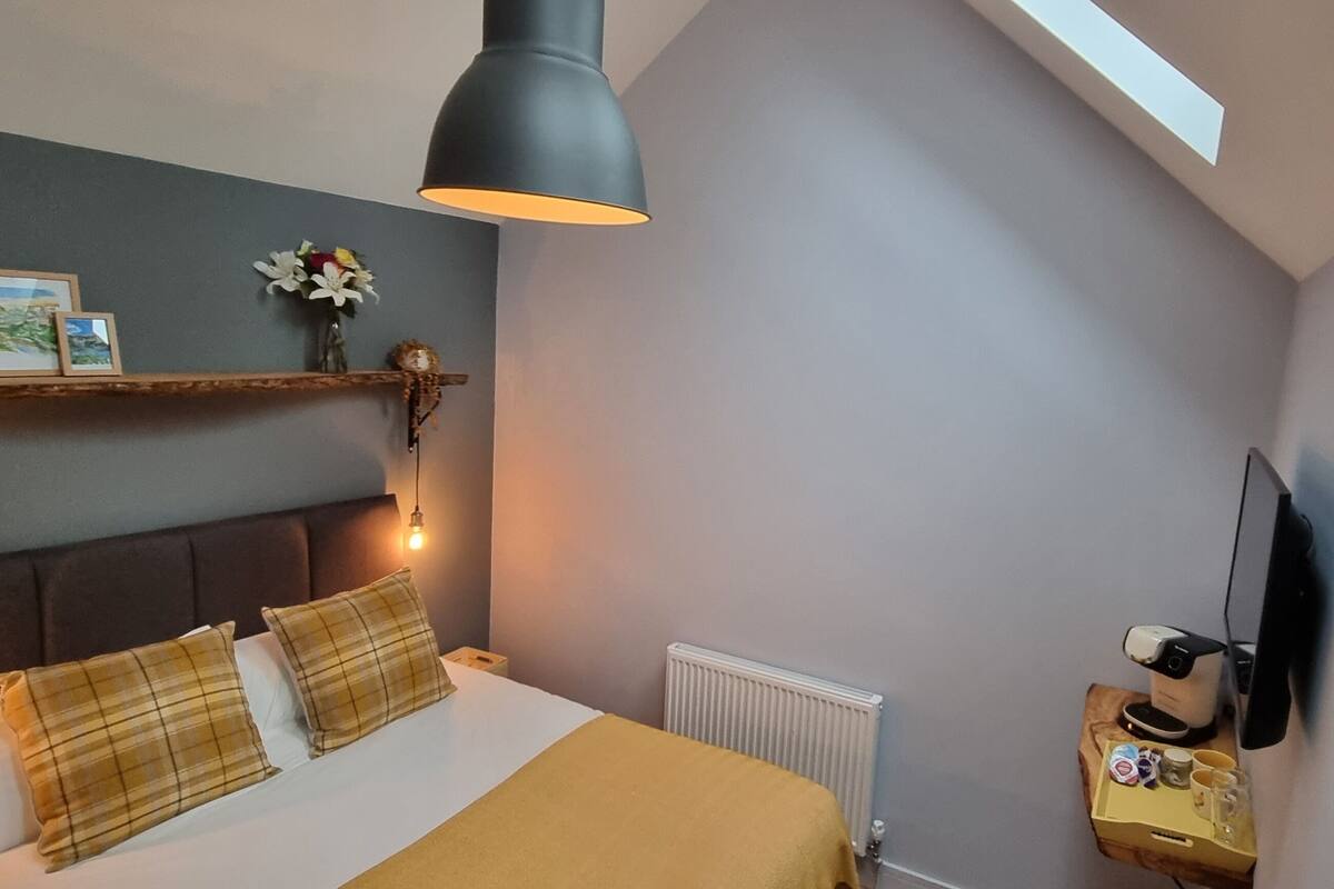 Ein Schlafzimmer mit einem Bett, einem an der Wand befestigten Fernseher, einem Nachttisch mit Lampe und einem Regal mit Dekoration.